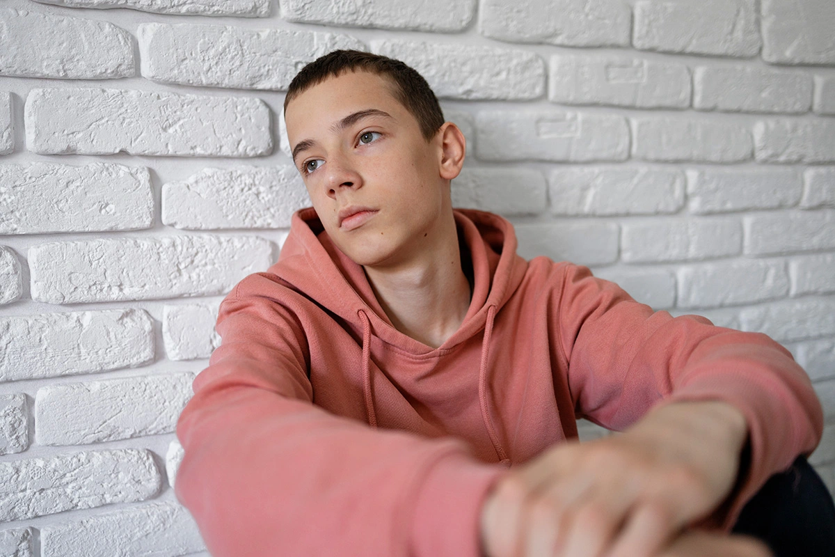 Adolescente apoyado en una pared blanca pensativo