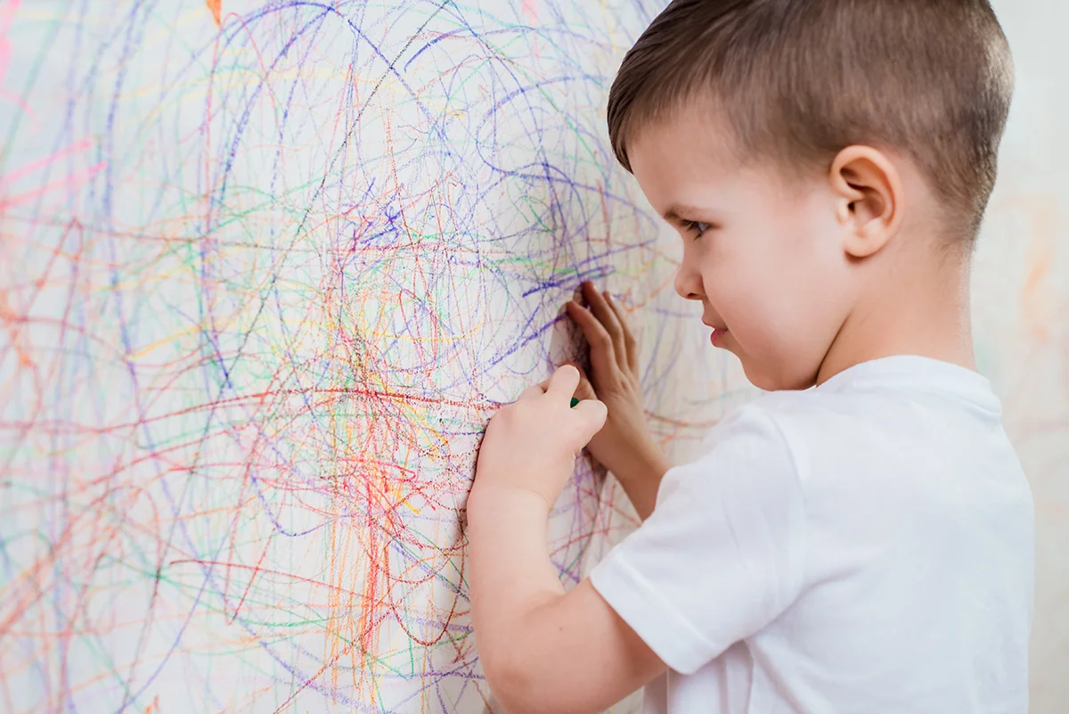 Niño pintando lineas de colores en una pared